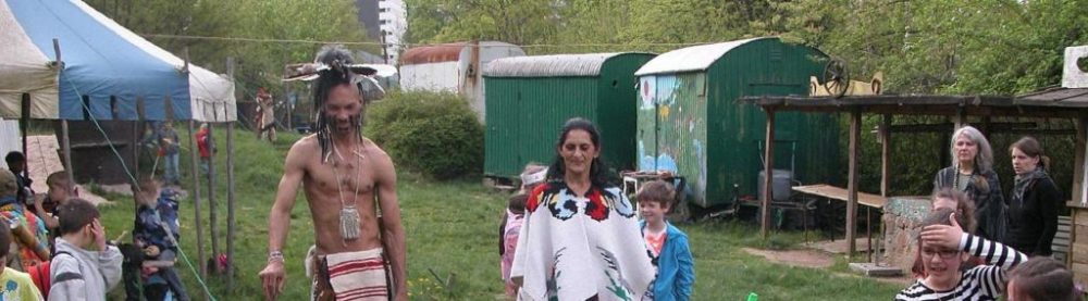Indianer stehen um ein Feuer, im Hinbtergrund Bauwägen
