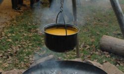 Sichere Feuerstelle. Darüber hängt ein Topf mit Suppe.