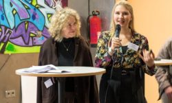 Zwei Frauen am Stehpult, eine spricht ins Mikrofon